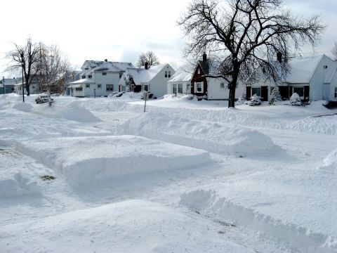 1975 Ford Torino - A residential street is covered in deep snow, with houses lining the sides and a single car partially obscured.