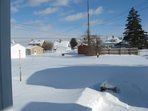 1975 Ford Torino - A vehicle is mostly buried in snow in a residential area during winter, with houses and utility lines visible under a blue sky.