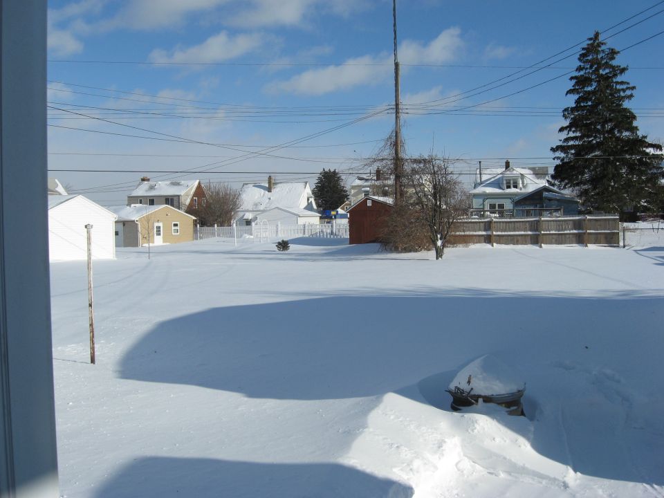 Snow-covered vehicle in a winter scene with houses and a tall pole