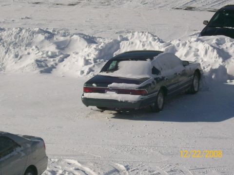 1995 Mercury Grand Marquis - A dark sedan is partially buried in snowdrifts, indicating a recent snowfall.