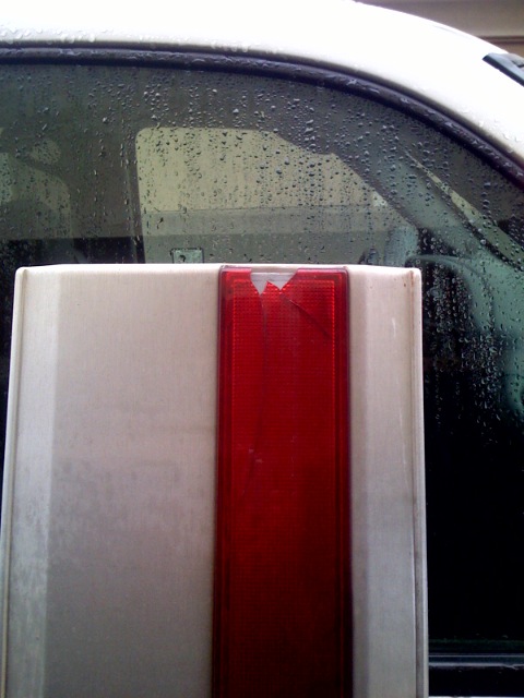 1987 Ford Bronco - Close-up of a damaged red taillight assembly on a white vehicle, with water on the window.