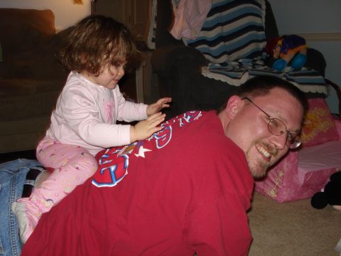 2000 Ford Crown Victoria - A man smiles as a young child sits on his back, playing indoors.
