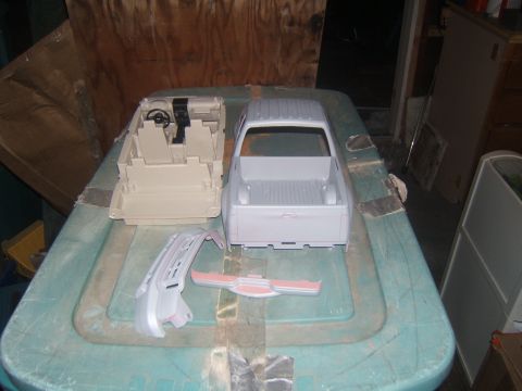 1988 Ford Bronco - A model truck body and interior are laid out on a teal plastic surface, along with separate bumper parts. The truck body is unpainted, and…
