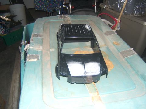 1988 Ford Bronco - A black plastic RC car body is placed on top of a teal plastic storage bin. The RC car body appears to be a Ford Bronco with a roof rack an…