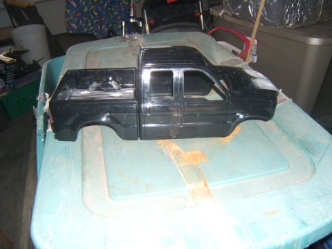1988 Ford Bronco - A black, four-door pickup truck body is shown from a 3/4 front angle, resting on a light blue plastic storage container.