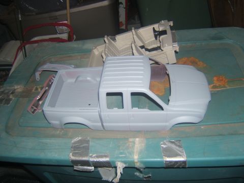 1988 Ford Bronco - A gray unpainted model truck body and interior are laid out on a teal plastic bin. The truck body is a pickup truck with a separate hood an…
