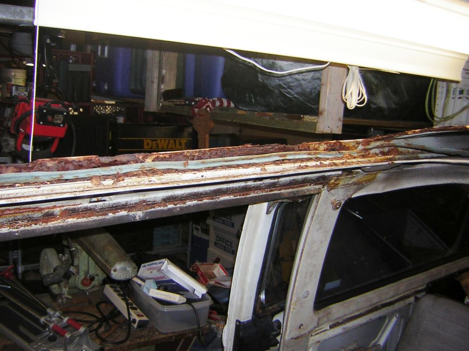 Rusted roof gutter and drip rail on white VW bus during bodywork in a garage