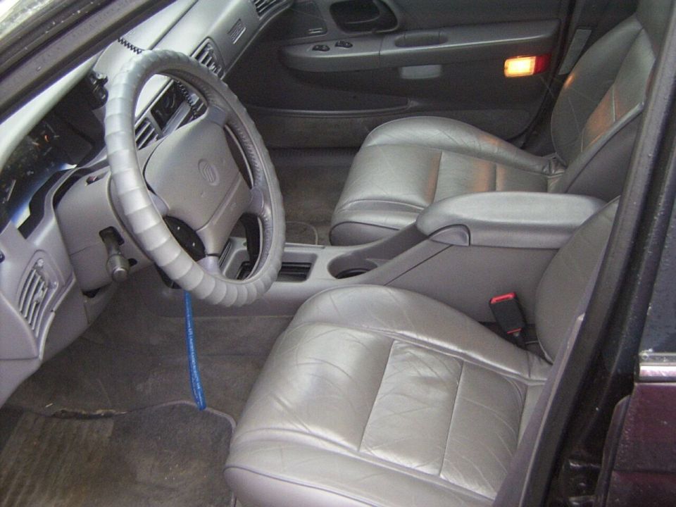 Car interior with gray leather seats, steering wheel, and dashboard. A blue cord hangs from the steering column