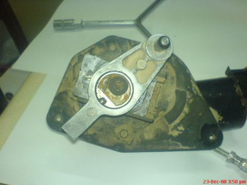 1992 Ford Crown Victoria - A windshield wiper motor and its gear-drive assembly with the cover removed, resting on white paper on a bench. The output gear, crank arm…