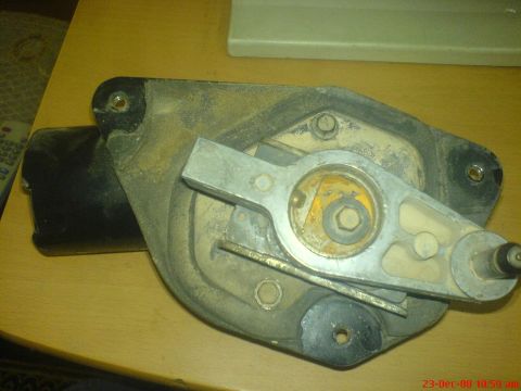 1992 Ford Crown Victoria - A wiper motor assembly sitting on a light wood table, with the aluminum crank arm bolted to the gearbox output shaft over yellowed old grea…