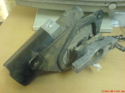 1992 Ford Crown Victoria - A complete wiper motor and linkage assembly propped on a wood desk in front of a CRT monitor, viewed from the side so the black motor can,…