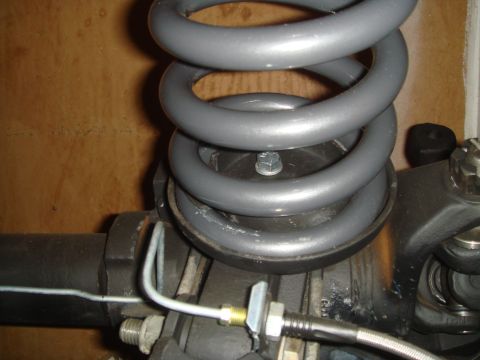 1992 Ford Bronco - A close-up view shows the top of a gray coil spring mounted on a black suspension component, likely part of a vehicle's axle. A brake line…