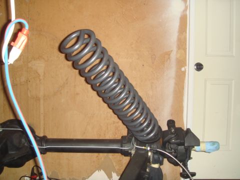 1992 Ford Bronco - A large gray coil spring is mounted to a black suspension component, possibly part of a vehicle's axle or steering system. A blue and white…