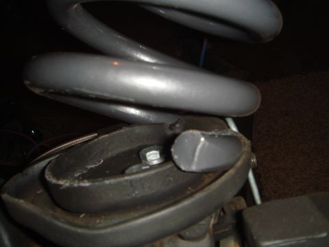 1992 Ford Bronco - A close-up view shows a gray coil spring resting on a black rubber or plastic mount. A silver bolt and washer are visible securing the moun…