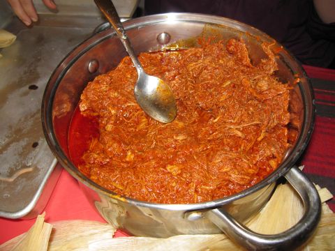 1986 Ford Bronco - A large pot of shredded meat in a red sauce is shown, with a spoon resting inside. Corn husks are visible at the bottom of the pot.