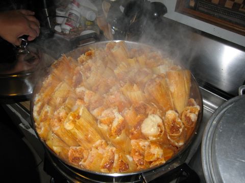 1986 Ford Bronco - A large pot filled with steaming tamales is shown in a kitchen setting. A hand is visible on the left, holding the lid of a smaller pot.