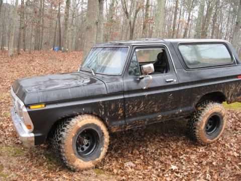 1978 Ford Bronco - A black 1978 Ford Bronco is parked on a dirt road covered in fallen leaves. The vehicle is heavily splattered with mud, indicating it has b…