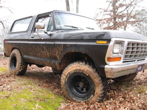 1978 Ford Bronco - A black 1978 Ford Bronco is shown from a low angle, covered in mud after off-roading. The vehicle has large, aggressive tires and is parked…