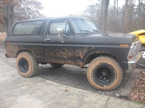 1978 Ford Bronco - A muddy black 1978 Ford Bronco is parked on a concrete surface with trees in the background. The vehicle has off-road tires and appears to…