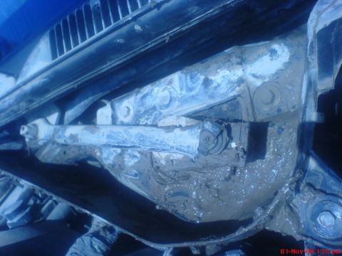 1992 Ford Crown Victoria - Underbody close-up of a vehicle's transmission and floorpan caked in thick wet mud, with the driveshaft tunnel, crossmember bolts and body…