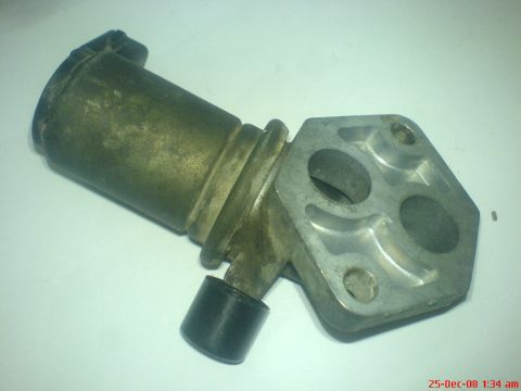 1992 Ford Crown Victoria - A removed idle air control valve photographed on a white surface, showing its cylindrical solenoid body with black end cap and connector, t…