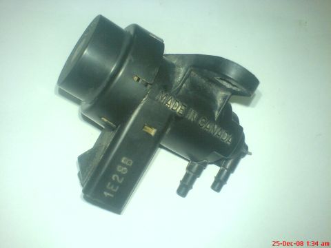 1992 Ford Crown Victoria - A removed black plastic vacuum solenoid valve on a white background, molded with MADE IN CANADA and the part code 1E26B on its body, with t…