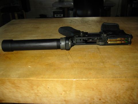1996 Ford Bronco - A firearm with a suppressor attached is resting on a wooden table. The firearm has a magazine inserted with two rounds of ammunition visibl…