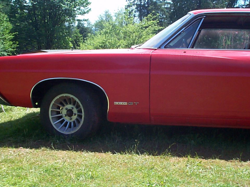Red 1968 Ford Galaxie side view showing front fender, GT badge and alloy wheel, parked on grass