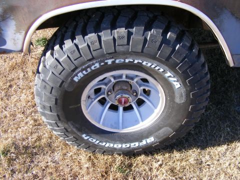 1979 Ford Bronco - A close-up, low-angle shot of a BFGoodrich Mud-Terrain T/A tire mounted on a light-colored multi-spoke wheel on a vintage vehicle. The tire…