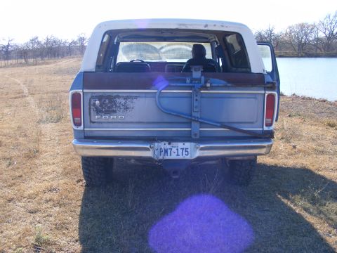 1979 Ford Bronco - The rear view of a light blue Ford Bronco with a white roof is parked on a grassy area next to a body of water. The vehicle has a visible T…