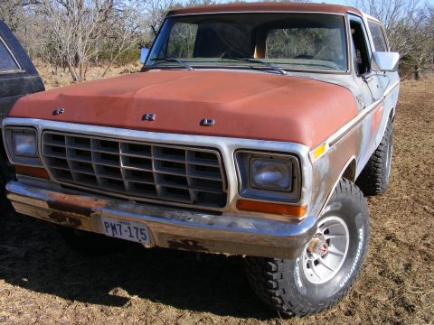 1979 Ford Bronco - A rusty, red and blue Ford Bronco is parked outdoors on a dirt lot. The front of the vehicle is visible, showing the grille, headlights, an…