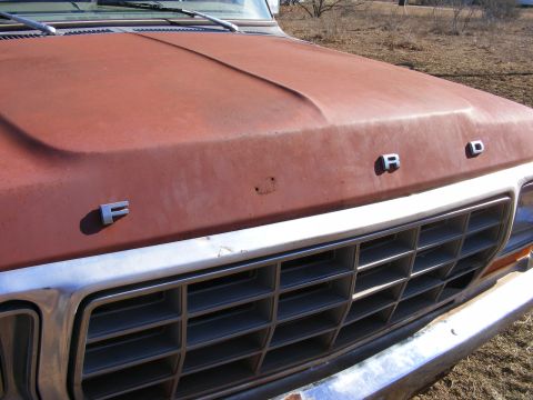 1979 Ford Bronco - The front view of a rusty red Ford truck hood shows the letters F, R, and D in chrome emblems. A chrome grille with horizontal bars is visi…