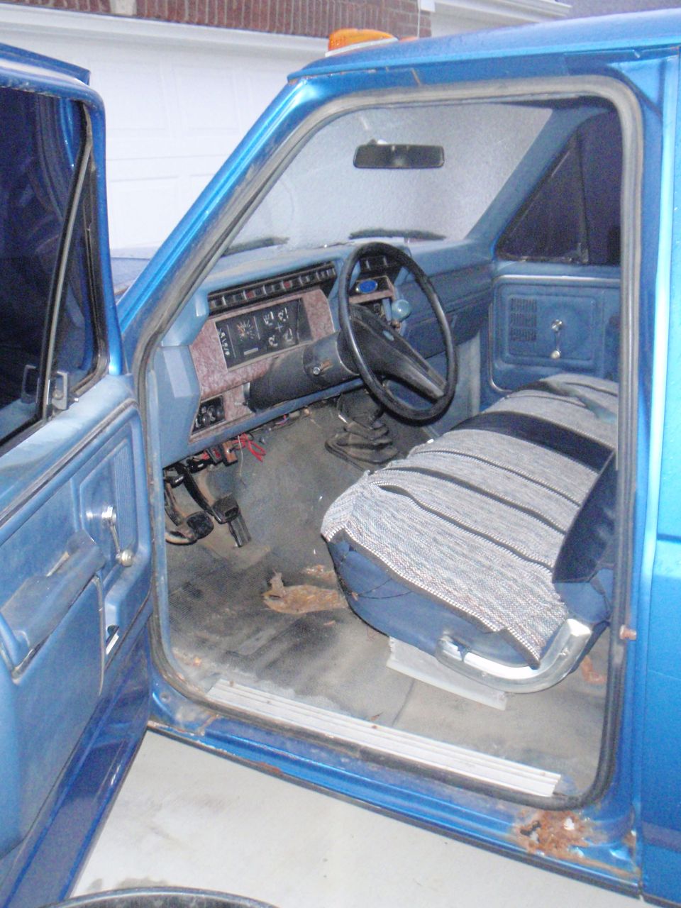 Interior of a blue 1985 Ford F-250 pickup truck, showing dashboard, steering wheel, and driver's seat.