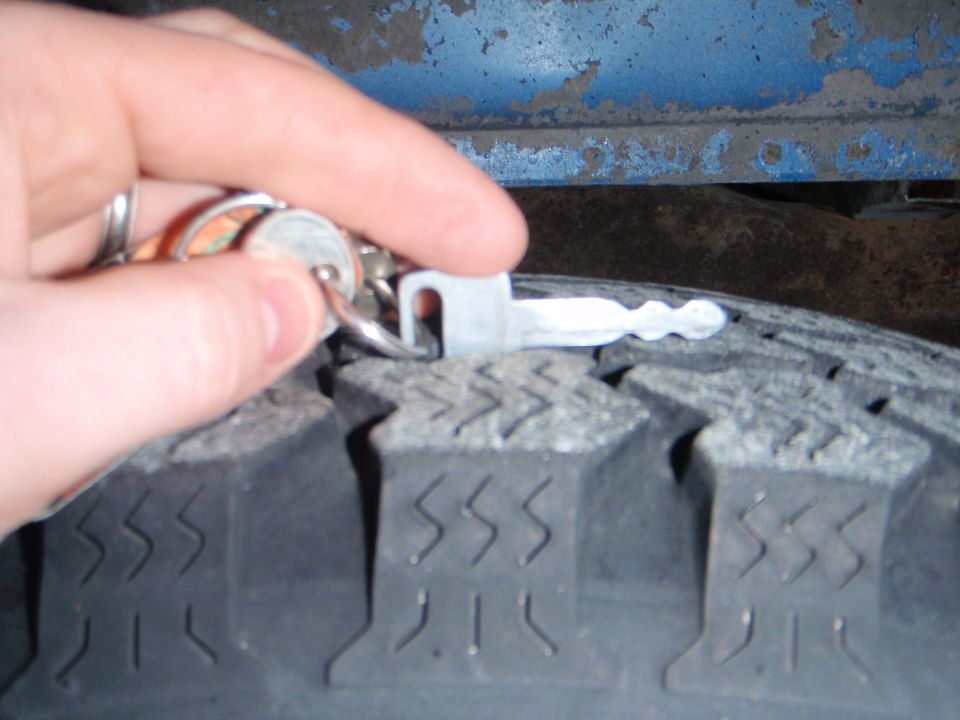 Hand holding a key near a tire tread.