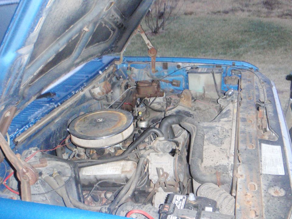 Dusty engine bay of a blue 1985 Ford F-250 with hood open.