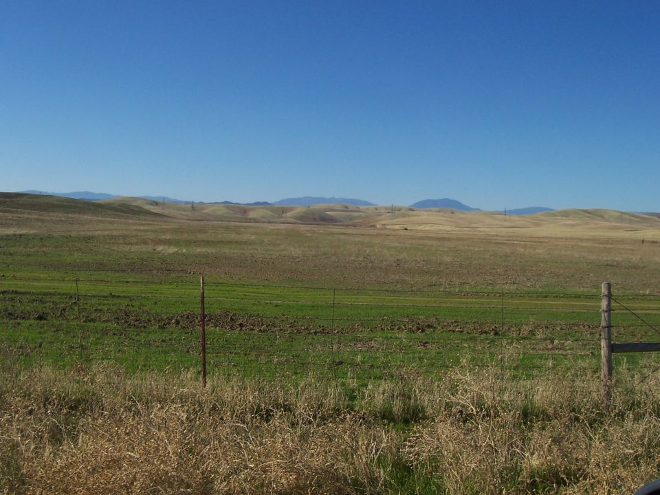 Rolling hills and fields with a fence in the foreground under a clear blue sky.