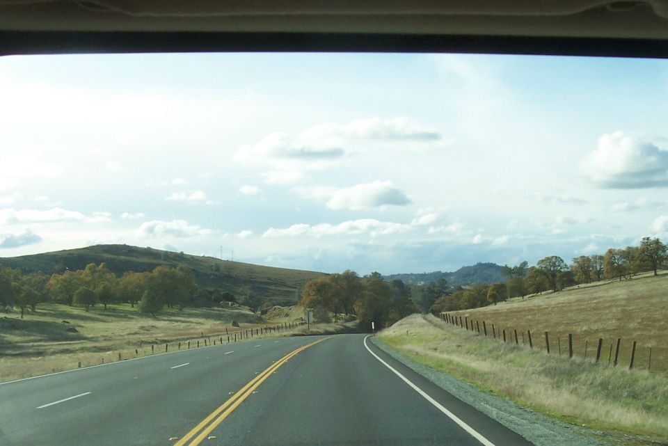 View from a car window of a highway curving through hills with trees and clouds.