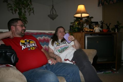 1990 Chevrolet Suburban - A man and a woman are sitting on a couch in a living room. The man is wearing a red t-shirt and the woman is wearing a white t-shirt and ho…