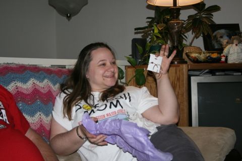 1990 Chevrolet Suburban - A woman is sitting on a couch and holding up a pair of earrings. She is wearing a white t-shirt and holding a piece of purple tissue paper.