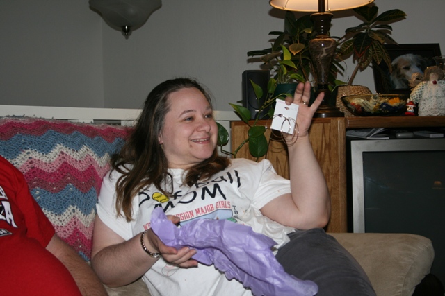 Woman holding earrings and purple tissue paper while sitting on a couch