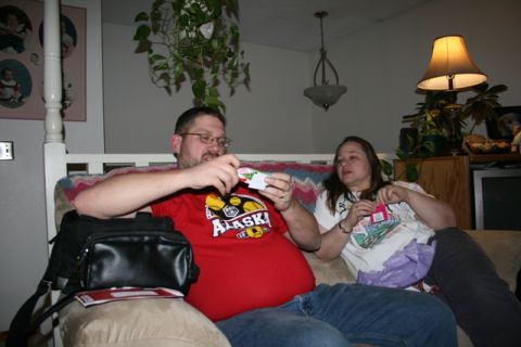 1990 Chevrolet Suburban - A man and a woman are sitting on a couch in a living room. The man is wearing a red t-shirt and holding a small object in his hands. The wo…