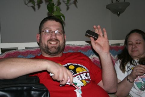 1990 Chevrolet Suburban - A man wearing glasses and a red t-shirt is holding a small silver object, possibly a phone, in his raised hand. A woman with her eyes close…