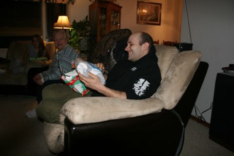 1990 Chevrolet Suburban - A man in a black hoodie is sitting in a recliner, smiling and holding a wrapped gift. Another person is sitting on a couch in the backgroun…
