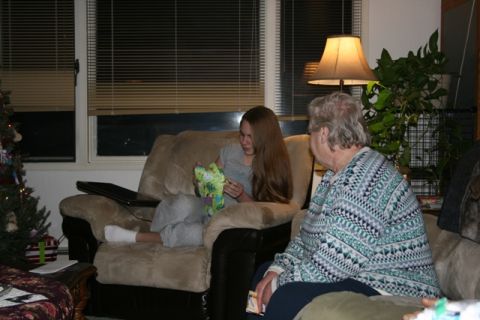 1990 Chevrolet Suburban - A young woman sits in a recliner opening a gift while an older woman watches her. A Christmas tree is visible to the left of the frame.