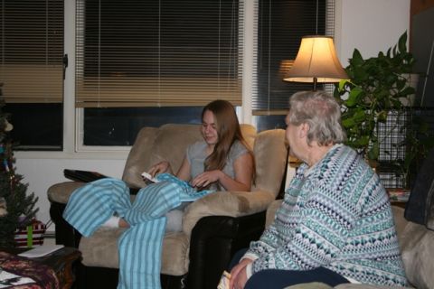 1990 Chevrolet Suburban - A young woman sits in a recliner, opening a gift of blue and white striped pajamas. An older woman sits next to her, looking away from the…