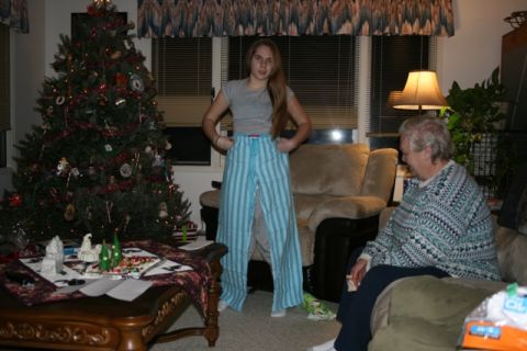 1990 Chevrolet Suburban - A young woman stands in a living room decorated for Christmas, wearing oversized striped pajama pants. An older person sits on a couch to t…