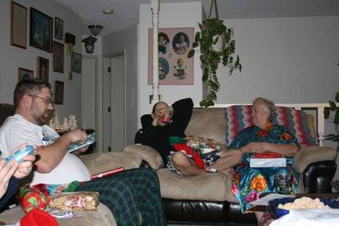 1990 Chevrolet Suburban - Three people are gathered in a living room, with gifts scattered around them. One man is opening a gift, another is drinking from a can, an…