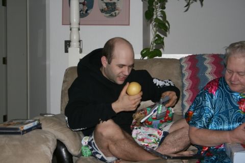 1990 Chevrolet Suburban - A man sits on a couch holding a yellow object and looking at a gift. Another person is seated next to him. The scene appears to be indoors,…