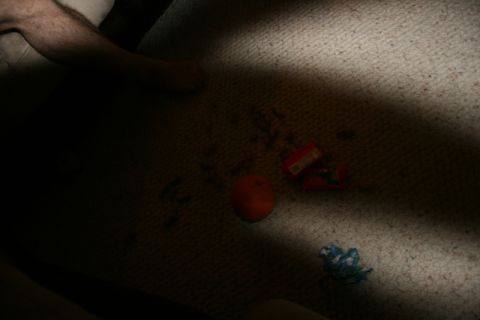 1990 Chevrolet Suburban - A close-up, low-angle shot of a carpeted floor with a few items scattered on it. Visible items include an orange, two small red candy wrapp…