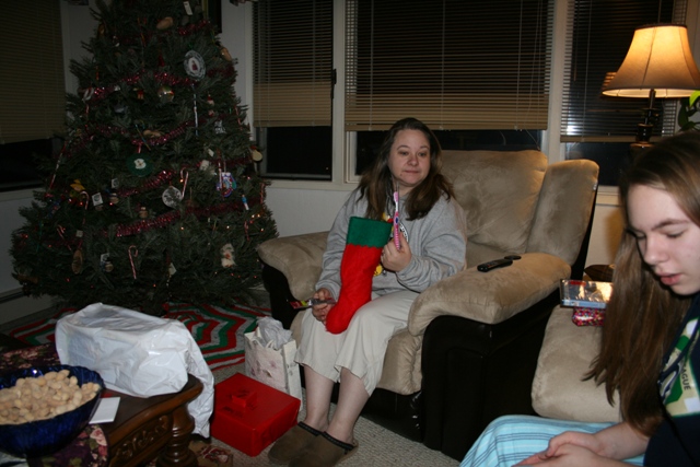Woman holding a Christmas stocking and toothbrush next to a Christmas tree.